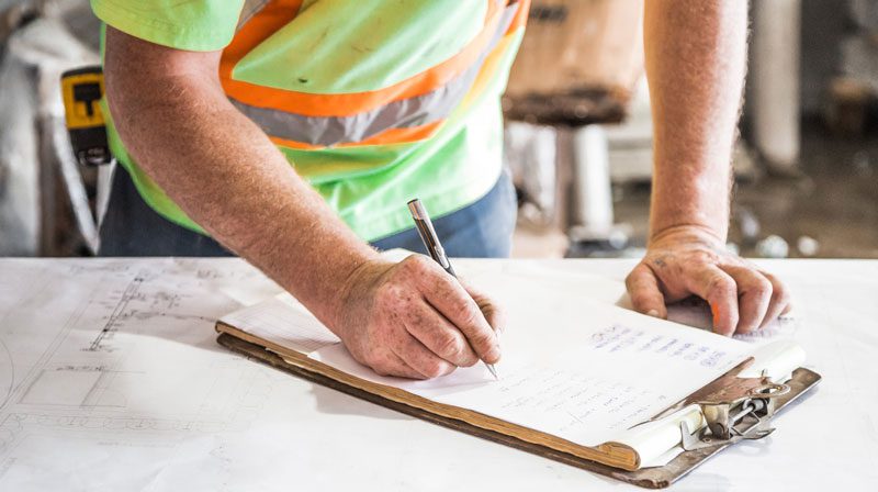 Safety Officer wearing a safety vest and writing on a clip board.